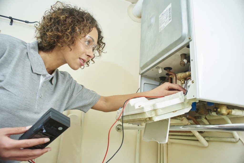 a female electrician is electrically testing a central heating boiler .