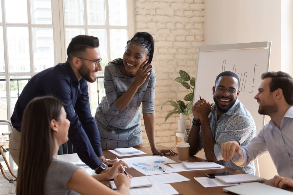 Happy friendly multiracial business team laughing working together at corporate briefing gathered at table, cheerful diverse office people group having fun talking enjoy teamwork during staff meeting