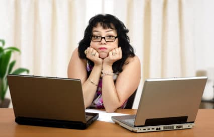 Glasses mature woman is boring on webinar on front of two laptops