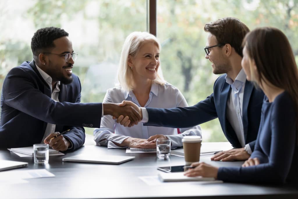 Smiling diverse businesspeople shake hands get acquainted greeting at team meeting in commercial real estate office, partnership