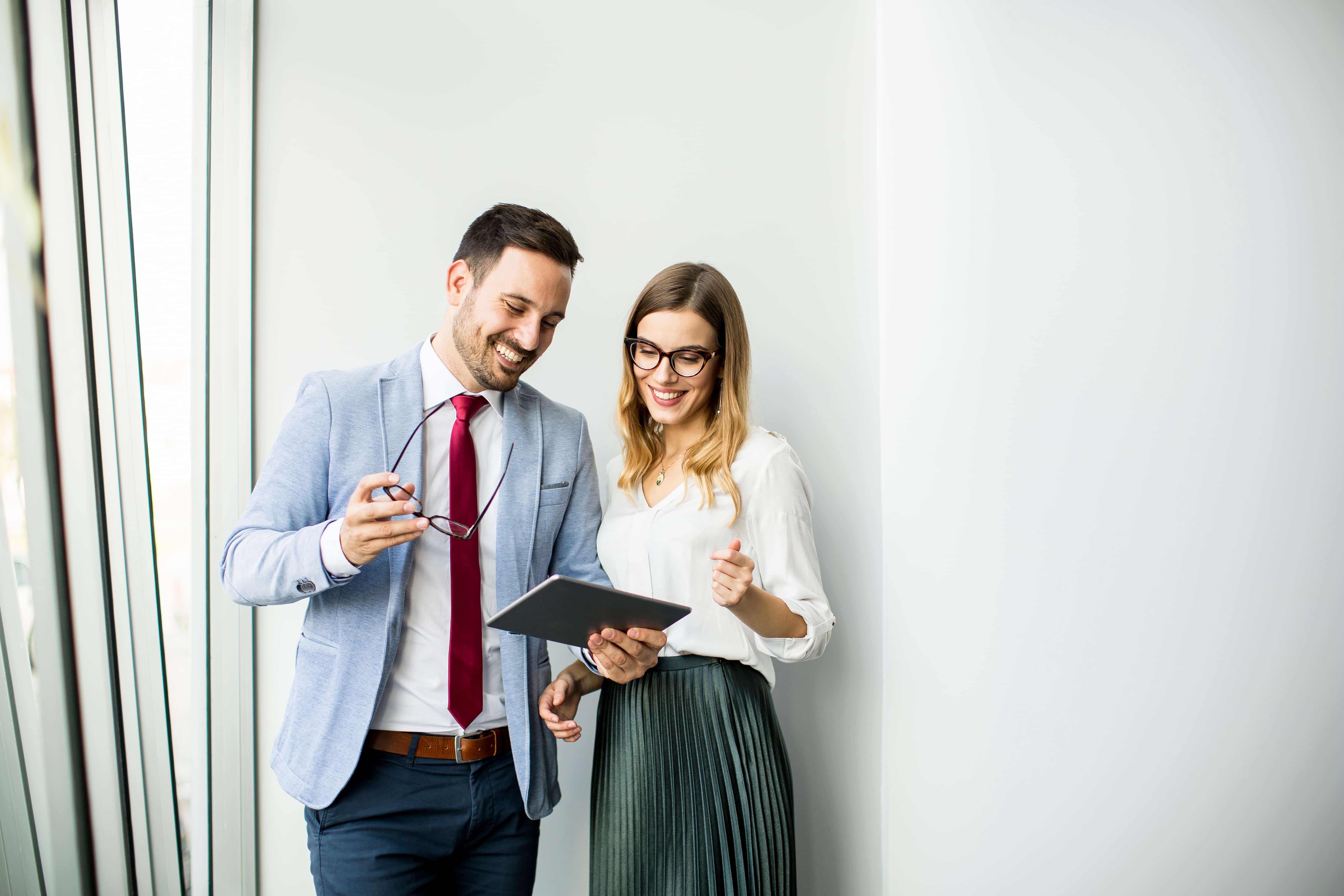 Happy business colleagues in modern office using tablet against wall