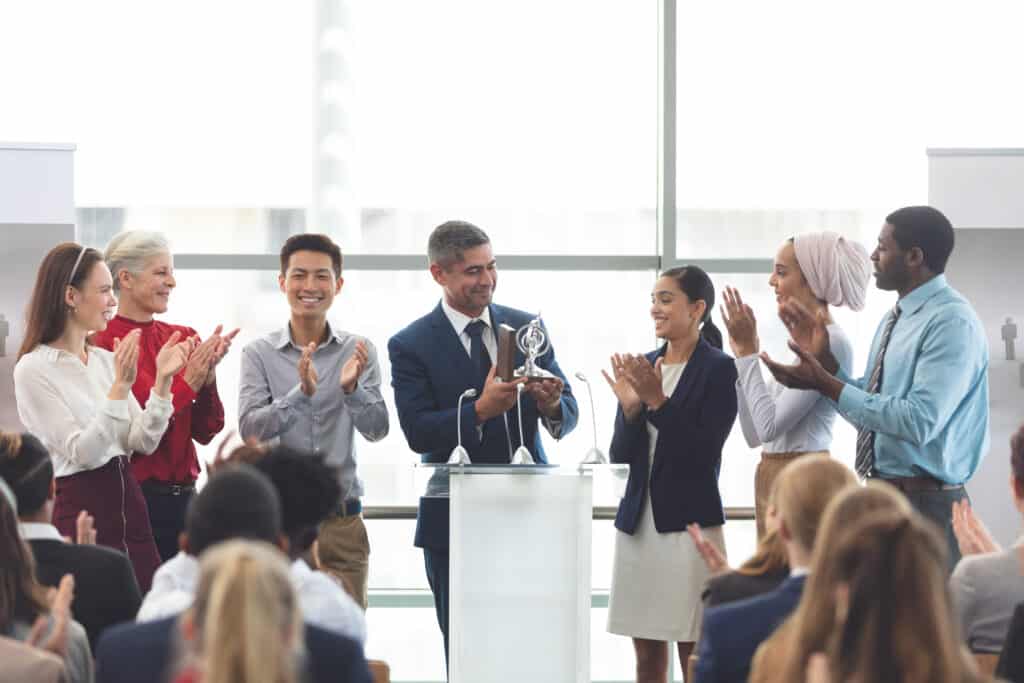 Businessman holding a kingsley excellence award for resident satisfaction at podium with colleagues