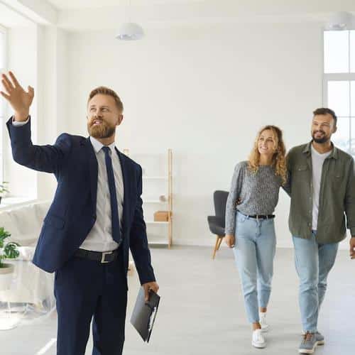 Real estate agent giving happy young customers a tour about a new spacious house