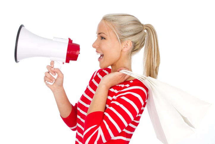 woman shouting into megaphone wearing bright red sweater and holding shopping bags as a sale concept
