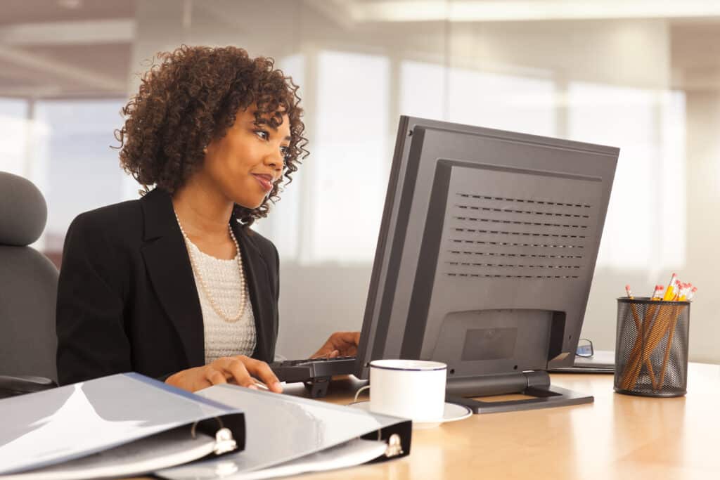 Young property management woman using computer at desk indoors office building to review policy management/policy compliance of her employees