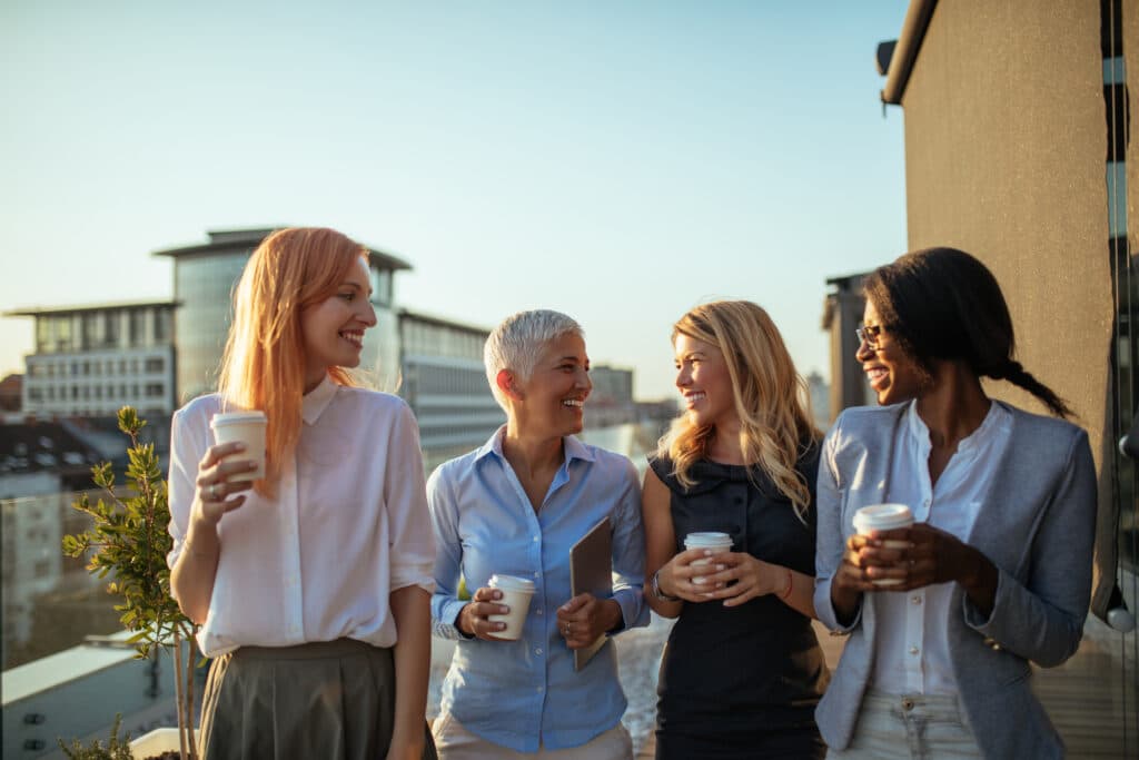 diverse group of women smiling at each other, holding coffee cups at their apartment community event
