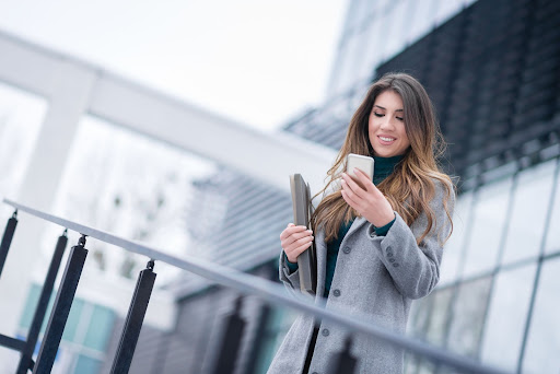 resident woman smiling at her phone outside her apartment taking a sms/text resident survey from grace hill