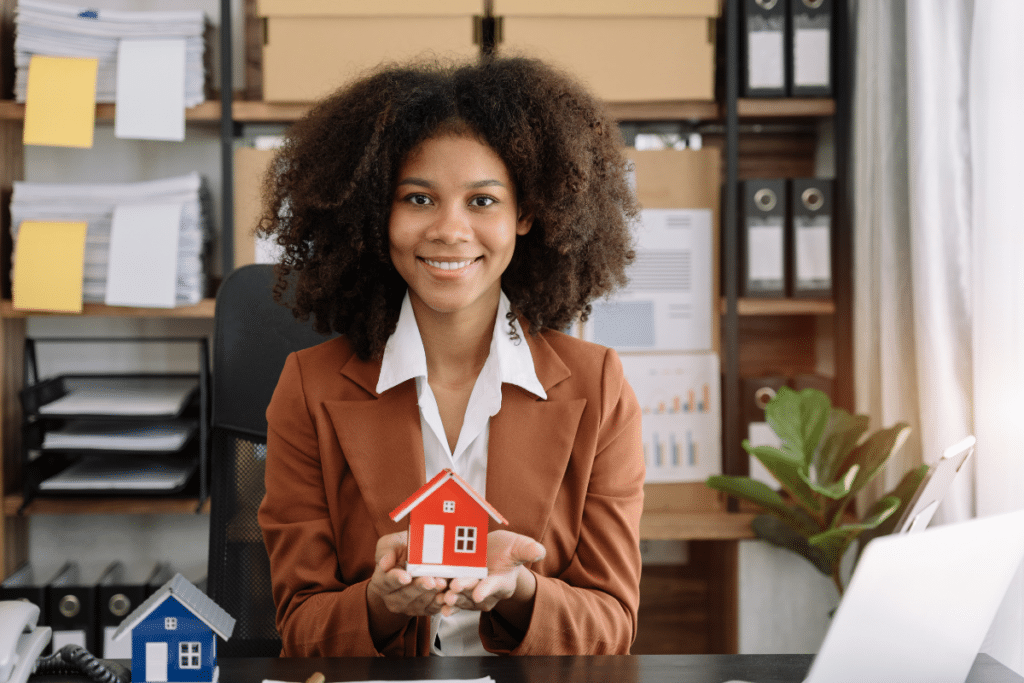 property manager woman holding little red house, smiling at the camera