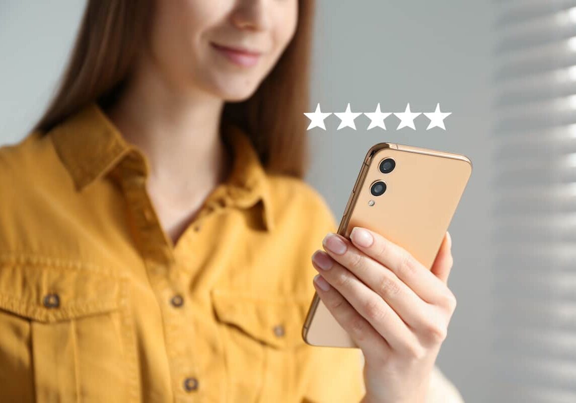 Woman leaving review online via smartphone indoors, closeup. Five stars over gadget