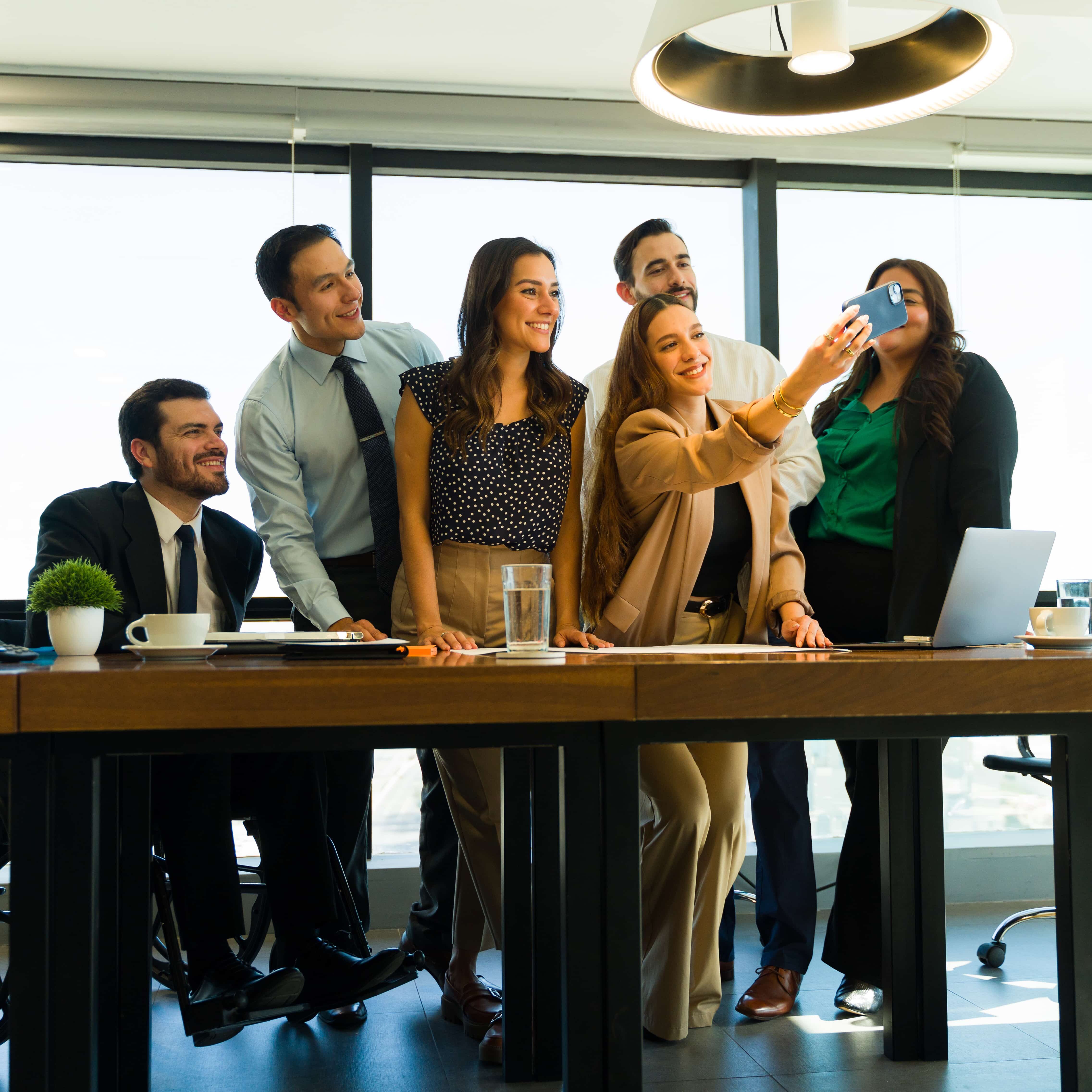 Inclusive group of businesspeople using a smartphone to take a selfie at the office